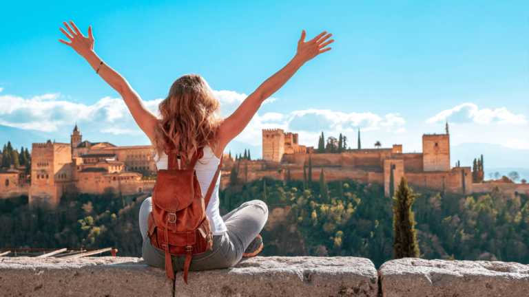 Foto van een vrouw die poseert met haar armen in de lucht voor het Alhambra in Granada