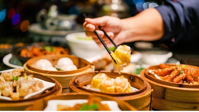 Traditionele Hong Kong dim sum geserveerd in bamboe mandjes, met een close-up van gestoomde siu mai die met stokjes wordt opgepakt.