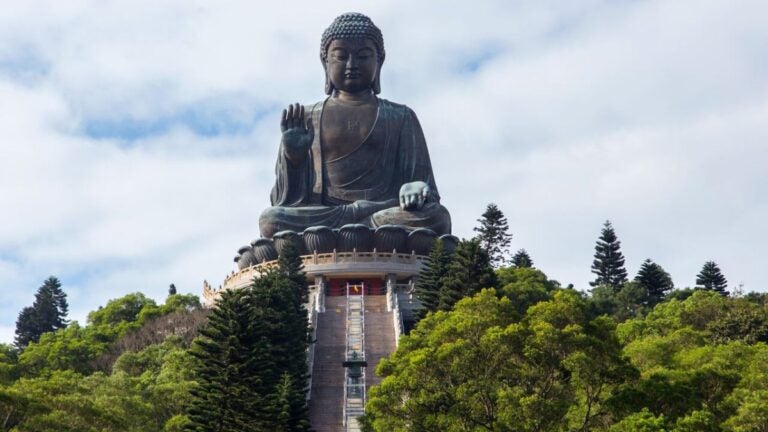 Het imposante bronzen Tian Tan Boeddha standbeeld op Lantau Island in Hong Kong, omringd door groene bergen onder een bewolkte hemel.