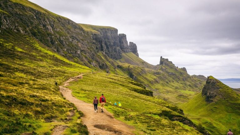 Wandelaars op een kronkelend zandpad langs de indrukwekkende groene kliffen van de Quiraing op Isle of Skye in Schotland.