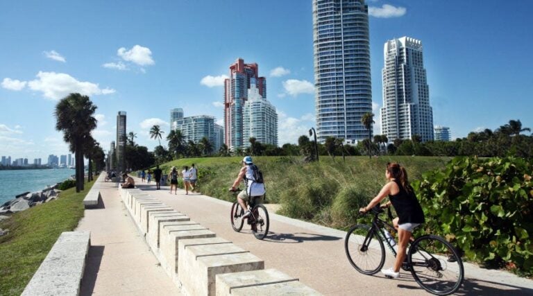 Mensen fietsen en wandelen langs de waterkant van Miami met skyline op de achtergrond.