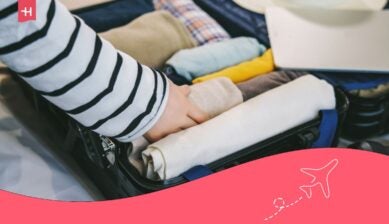 Iemand pakt een koffer in met netjes opgerolde kleding voor een reis naar Vietnam, voorzien van een roze grafische header en een vliegtuigicoon.