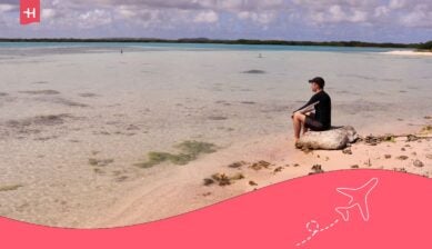 Reiziger zittend aan het strand van Bonaire met helder turquoise water, symbool voor zorgeloos internet en roaming tijdens je verblijf op het eiland.