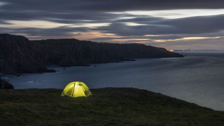 Een verlichte tent tijdens het wildkamperen in de Schotse natuur bij zonsondergang.