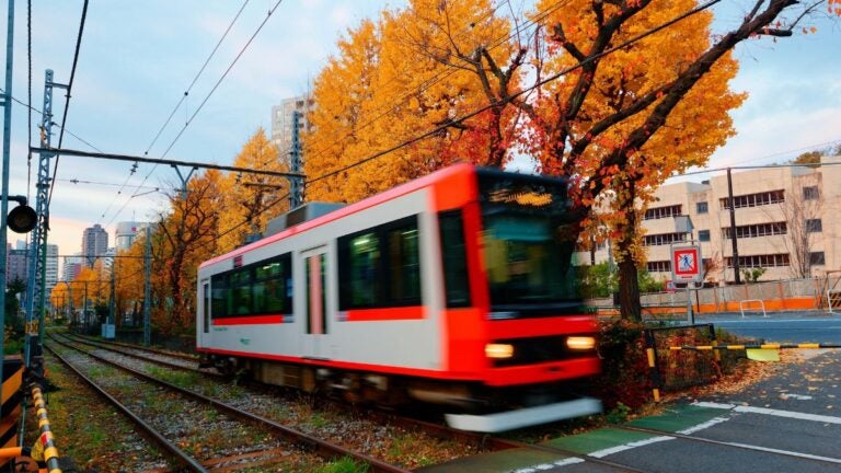 Tram van het openbaar vervoer in Tokyo die door een wijk rijdt met herfstkleuren op de achtergrond.
