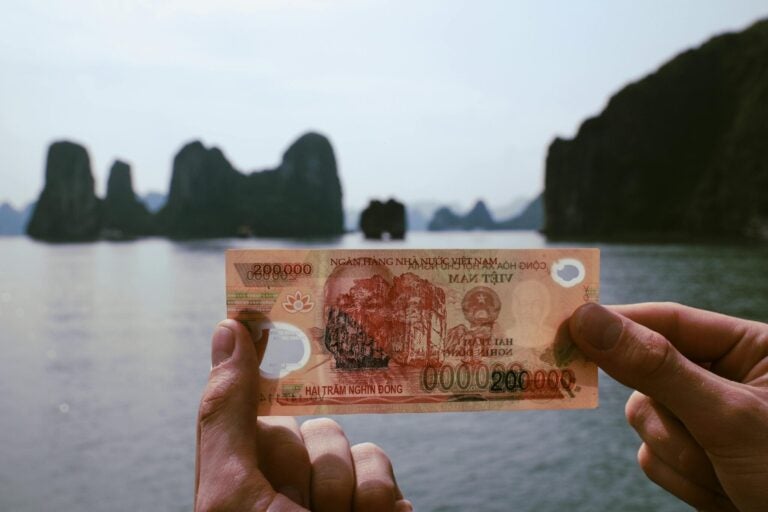 Iemand houdt een bankbiljet van 200.000 Vietnamese Dong vast tegen de achtergrond van de baai van Ha Long.
