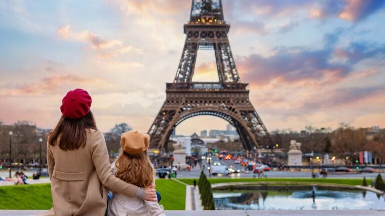 Een vrouw en een kind met baretten kijken uit over de Eiffeltoren in Parijs tijdens een sfeervolle zonsondergang, een van de beste stedentrips Europa.