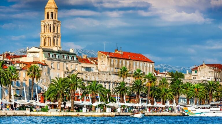 Een levendig uitzicht op de boulevard van Split met palmbomen en de historische Sint-Domniuskathedraal aan de Adriatische kust, een zonnige aanrader voor de beste stedentrips Europa.