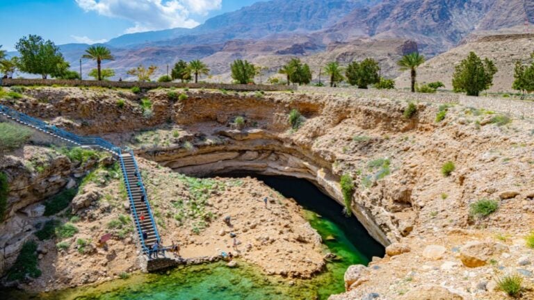 Het spectaculaire Bimmah Sinkhole in Oman met helder turquoise water en een stenen trap die naar beneden leidt in het kalksteen.