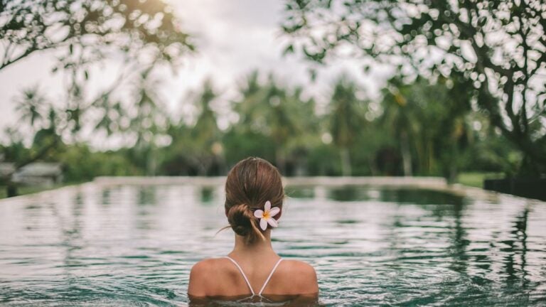 Een vrouw met een bloem in haar haar geniet van het uitzicht op de weelderige groene jungle vanuit een infinity pool in Maleisië.