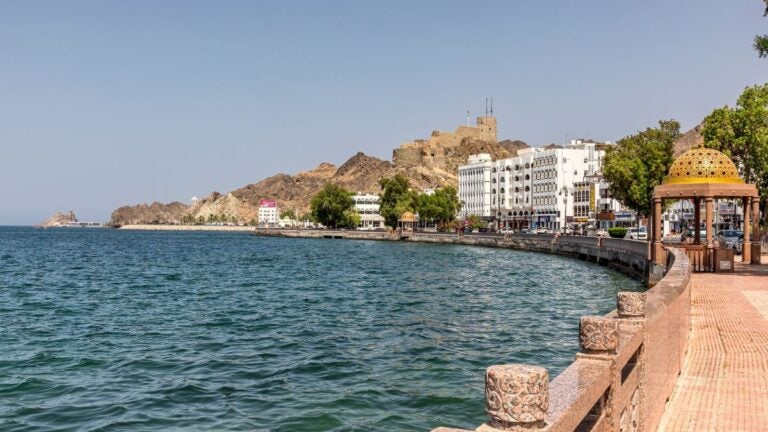Uitzicht over de Muttrah Corniche in Muscat, Oman, met de boulevard langs de zee en een historisch fort op de achtergrond.