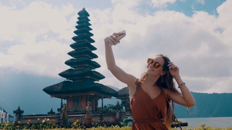 Een vrouw met zonnebril maakt een selfie voor de iconische Ulun Danu Beratan watertempel op Bali, Indonesië