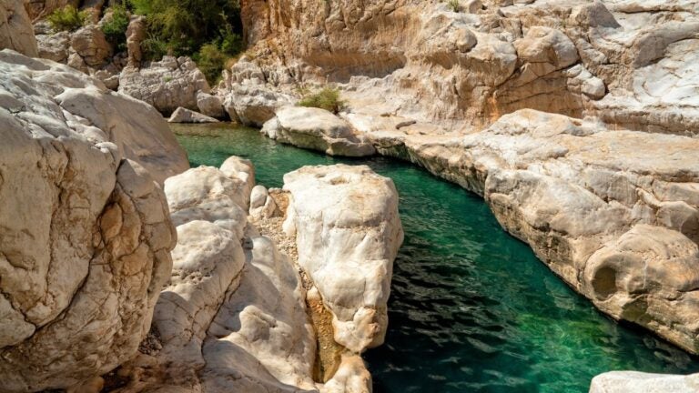 Kristalhelder groen water dat door de gladde witte rotsformaties van Wadi Bani Khalid in Oman stroomt