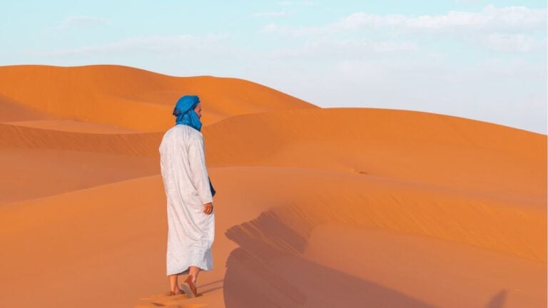 Een man in traditionele Omaanse kleding die over de uitgestrekte oranje zandduinen van Wahiba Sands wandelt