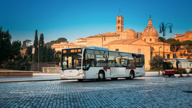 Stadsbus rijdt door Rome bij zonsondergang langs historische bezienswaardigheden.