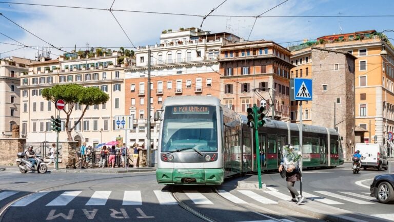 Tram rijdt door een kruispunt in Rome met historische gebouwen op de achtergrond.