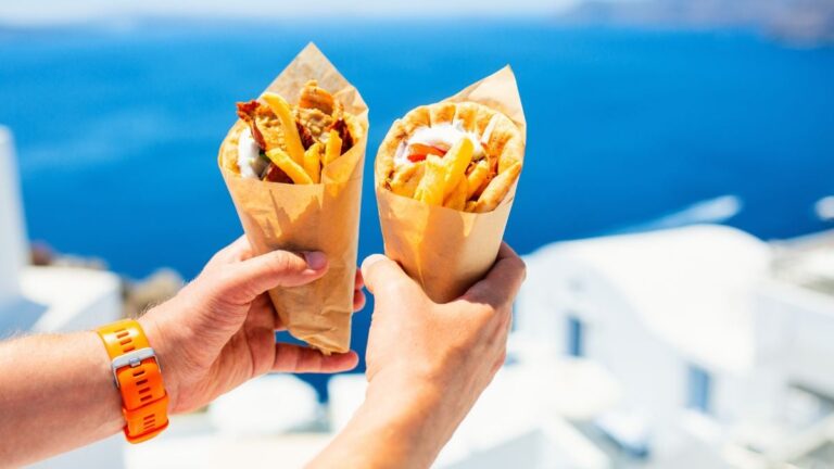 Twee gyros-pita’s met friet en vlees, vastgehouden met uitzicht op de Griekse zee.