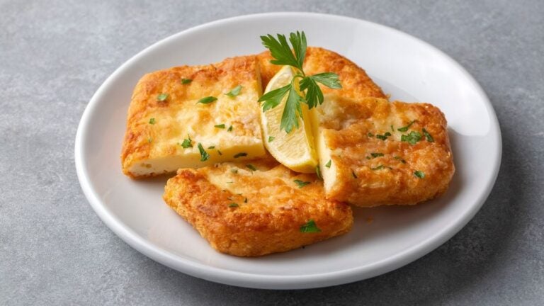 Gebakken saganaki-kaas met citroen en peterselie op een wit bord.