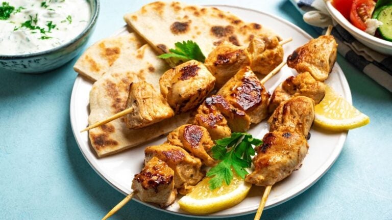 Kip-souvlaki met pitabrood, citroen en tzatziki op een bord.