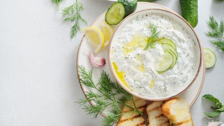 Tzatziki met komkommer, dille en gegrild brood op een lichte ondergrond.