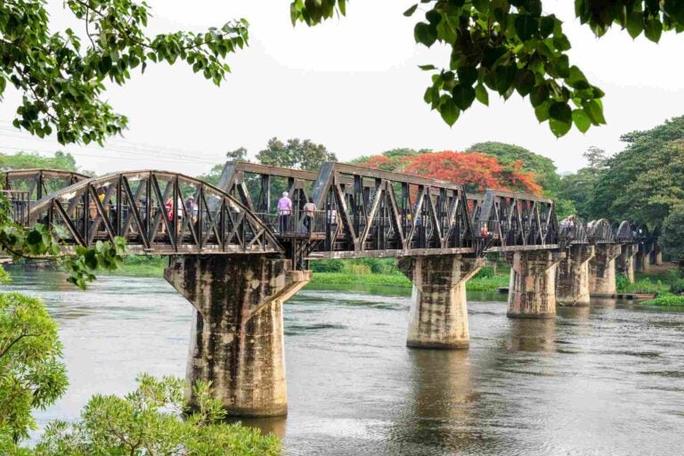 Bezoekers lopen over de historische brug over de River Kwai in Kanchanaburi, Thailand.