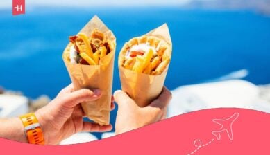Twee gyros-pita’s met friet en vlees, vastgehouden met uitzicht op de blauwe zee in Griekenland.