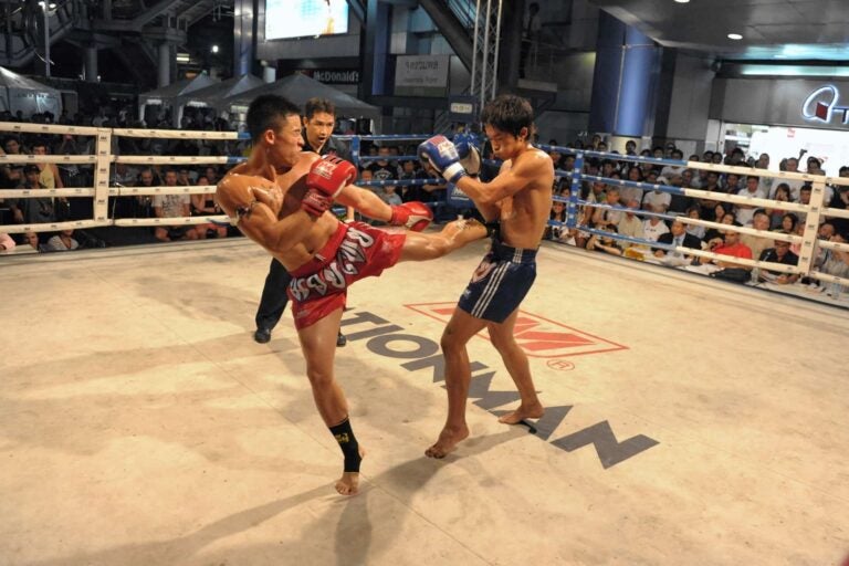 Twee vechters tijdens een Muay Thai-wedstrijd in een boksring in Thailand, omringd door toeschouwers.