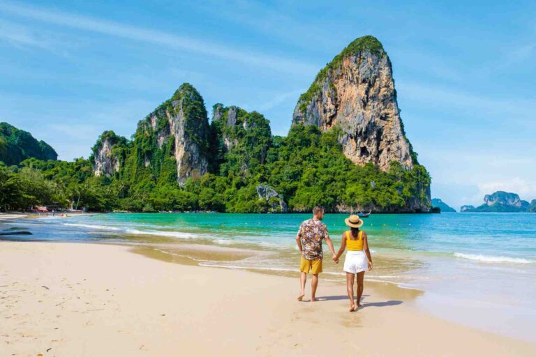Reizigers wandelen op Railay Beach in Krabi, met kalkstenen kliffen en helder blauw zeewater.