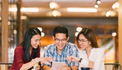 カフェでスマートフォンやタブレットを見ながら楽しそうに話す3人の友人