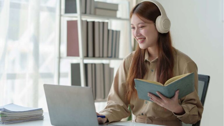 ヘッドホンをつけてノートパソコンを見ながらオンライン学習をする若い女性。