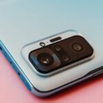 ピンクの背景に置かれたスマートフォンの背面カメラ部分。洗練されたデザインと先進的なカメラユニットが印象的。