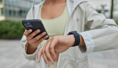 スマートフォンとスマートウォッチを見ながら、外出先で通信状況を確認する女性の様子