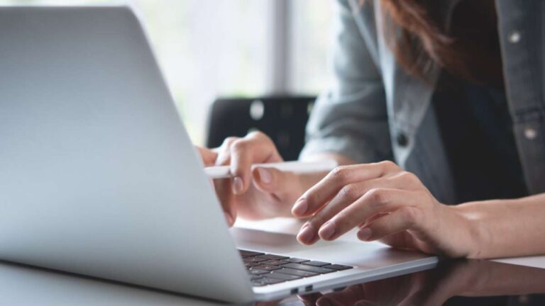 ノートパソコンをスタイラスペンで操作する女性の手元のクローズアップ。静かな環境で作業やデザインに集中している様子。