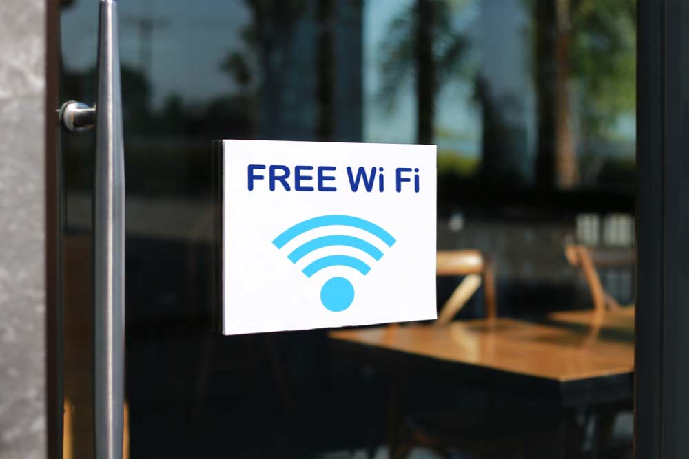 カフェのガラス扉に貼られた「FREE WiFi」と書かれたサイン。青いWiFiマークとともに、店内のテーブルと椅子が背景に見える。