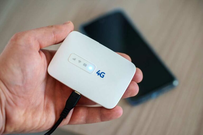 手に持たれた白い4GポケットWiFi端末。背景にはスマートフォンがぼんやりと映っており、インターネット接続の準備が整っている様子。