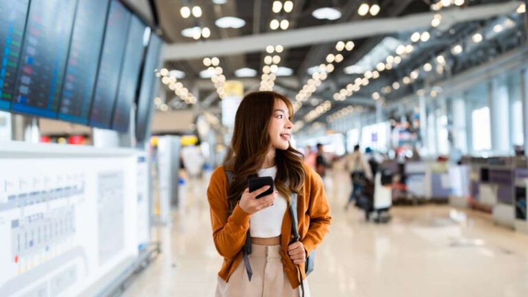 空港の出発ロビーでスマートフォンを手にフライト情報を確認する女性旅行者。