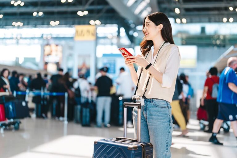 空港でスーツケースをそばに置き、スマートフォンを手にする旅行者