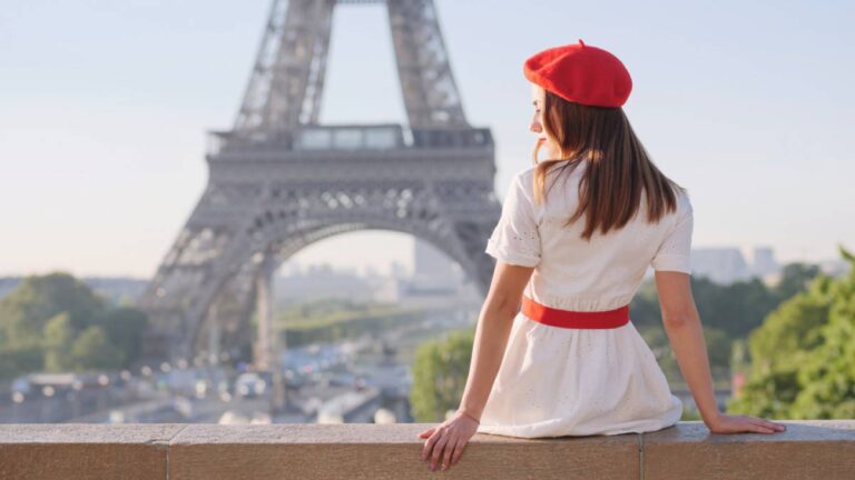 エッフェル塔を背景に赤いベレー帽と白いワンピースを着た女性が座って景色を眺めている後ろ姿。