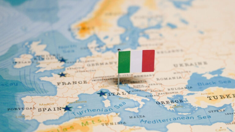 ヨーロッパの地図上に立てられたイタリアの国旗ピン。フランス、スペイン、ドイツ、ギリシャなど周辺の国々も表示されており、イタリアの位置が一目でわかる。