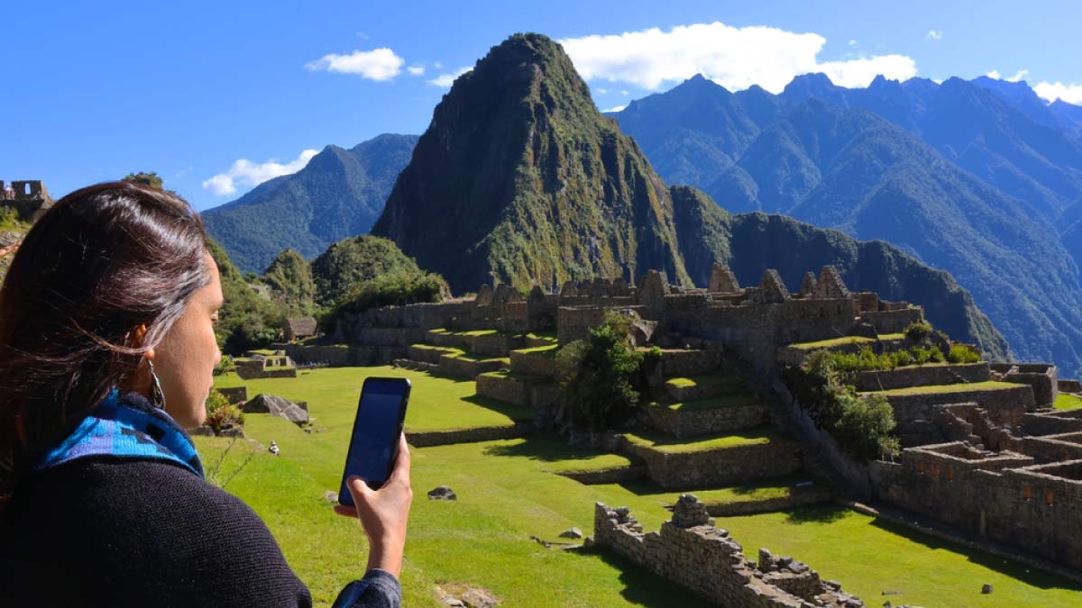 ALT ペルー・マチュピチュ遺跡を背景に、スマートフォンを手に風景を眺める女性