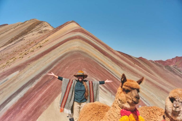 ペルーのレインボーマウンテンで、アルパカと一緒にポンチョを羽織ってポーズを取る旅行者