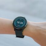 スマートウォッチを装着した手首。ディスプレイには18:34の時刻と心拍数、歩数などのフィットネスデータが表示されている。