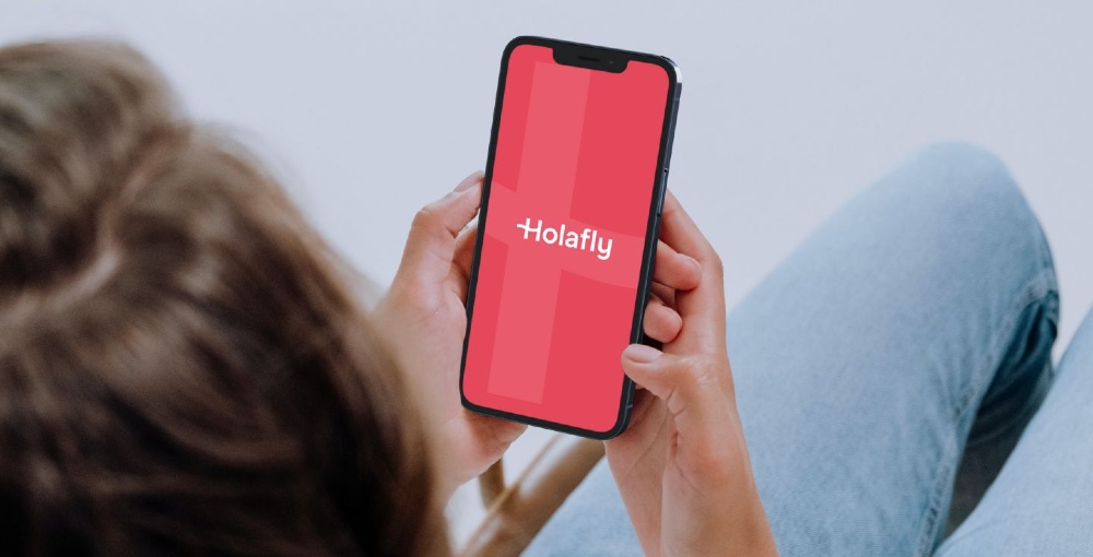 Holaflyのアプリが表示されたスマートフォンを手に持つ人物の画像。