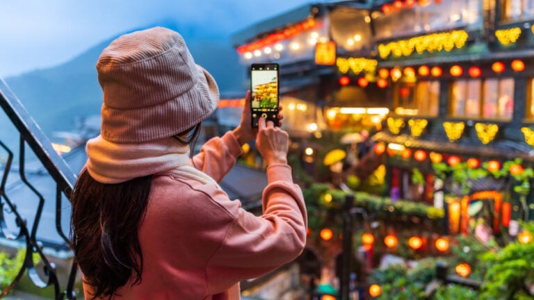 台湾・九份で夜景をスマートフォンで撮影する女性旅行者の後ろ姿