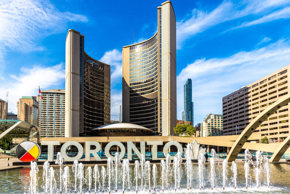 トロント市庁舎前のネイサン・フィリップス・スクエア。噴水と『TORONTO』の大型サインが青空の下で映える風景。