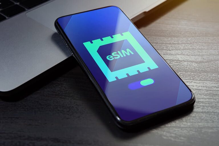 デスク上のノートパソコンの横に置かれたスマートフォン画面に、eSIMのアイコンと設定スイッチが表示されている様子