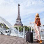 エッフェル塔を背景にスーツケースを持って橋の上に立つ女性旅行者