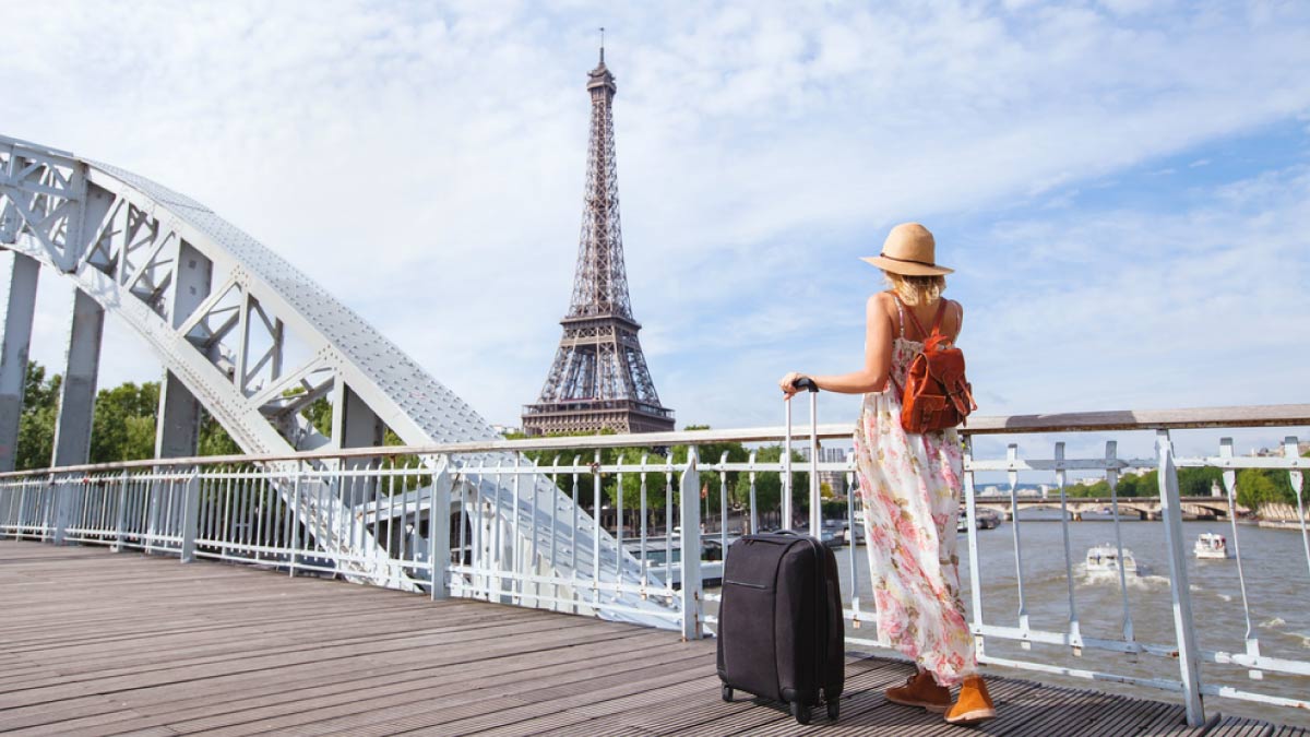 エッフェル塔を背景にスーツケースを持って橋の上に立つ女性旅行者