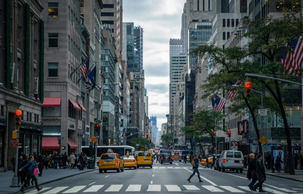 ニューヨーク市の街路風景。高層ビルが立ち並び、イエローキャブや歩行者が交差点を行き交う様子が見られる。