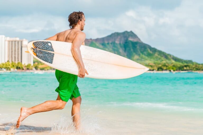 ワイキキビーチでサーフボードを持ちながら海へ向かうサーファーとダイヤモンドヘッドの景色
